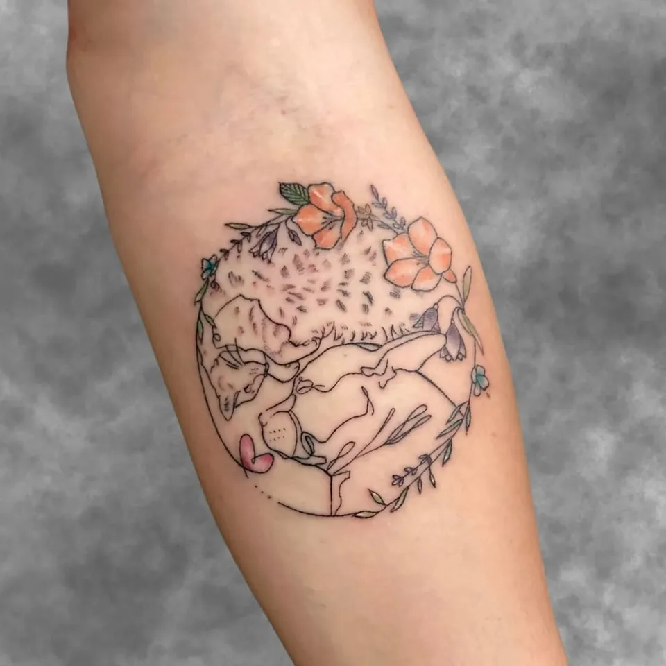 Tatuaje en línea fina de un gato dormido rodeado de flores dentro de un círculo, en el antebrazo, por Jenn Tatts