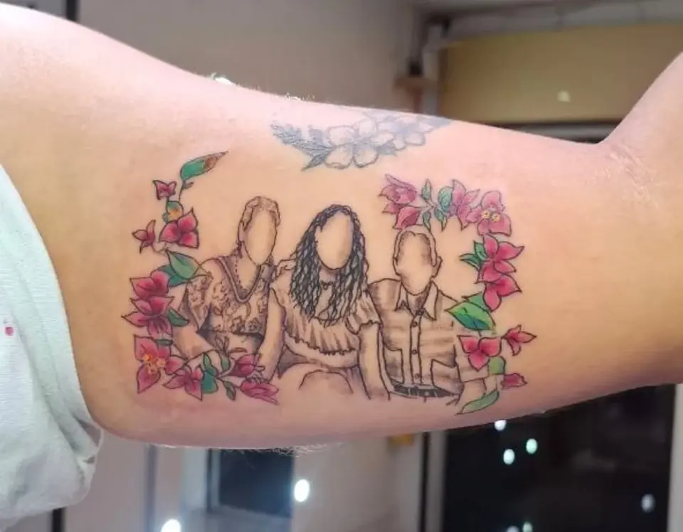 Tatuaje homenaje con las siluetas de una familia rodeada de flores, en el brazo, por Kewyn Romero
