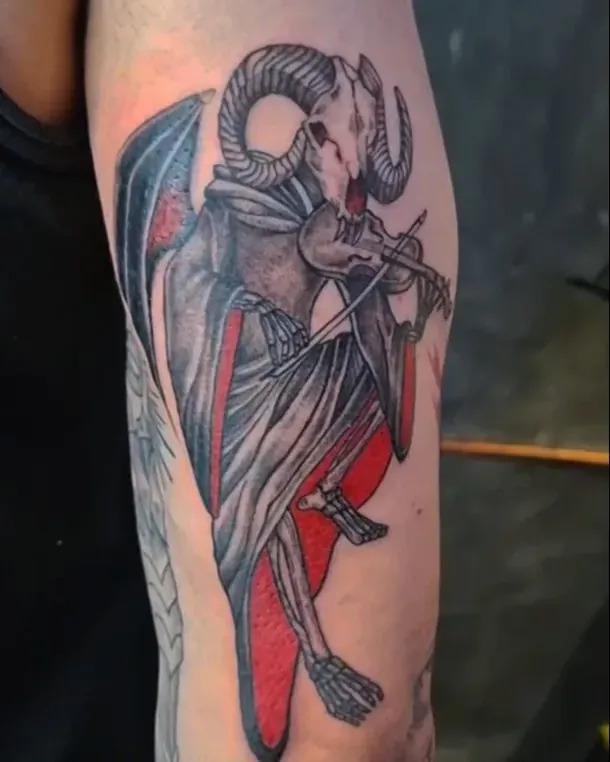 Tatuaje en black and grey de una figura con cuernos de carnero y una capa roja, en el brazo