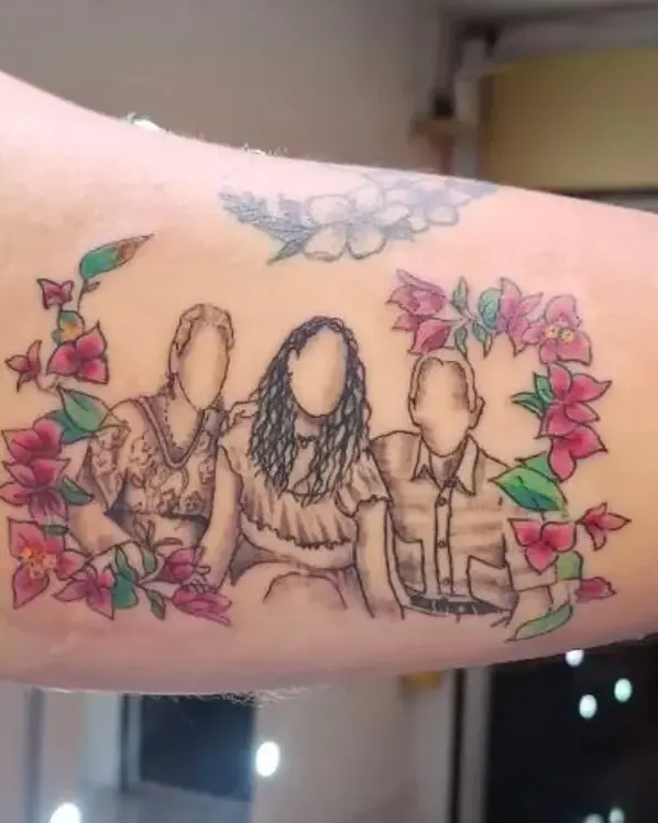 Tatuaje homenaje con las siluetas de una familia rodeada de flores, en el brazo