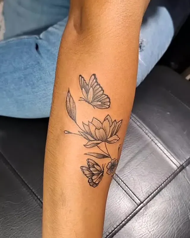 Tatuaje en línea de una flor de loto con mariposas en el antebrazo