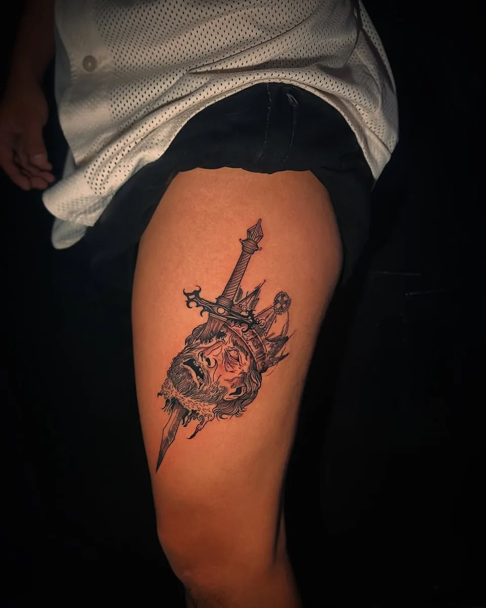 Tatuaje en black and grey de una daga con un cráneo y una corona, en el muslo, por Victor Hugo