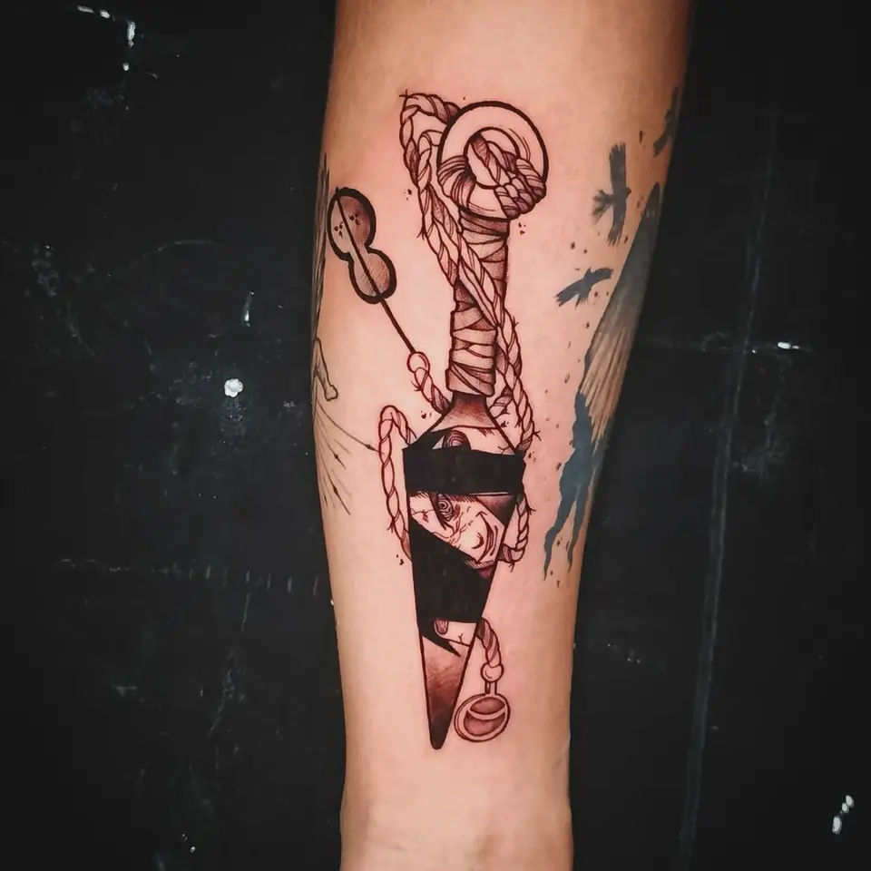 Tatuaje de estilo tradicional con una daga envuelta en cuerda y detalles en rojo, en el antebrazo, por Victor Hugo